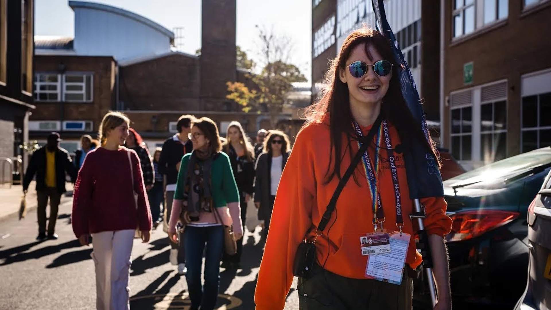 Student ambassador, in bright orange hoodie and sunglasses, leads a tour of the Llandaff Campus