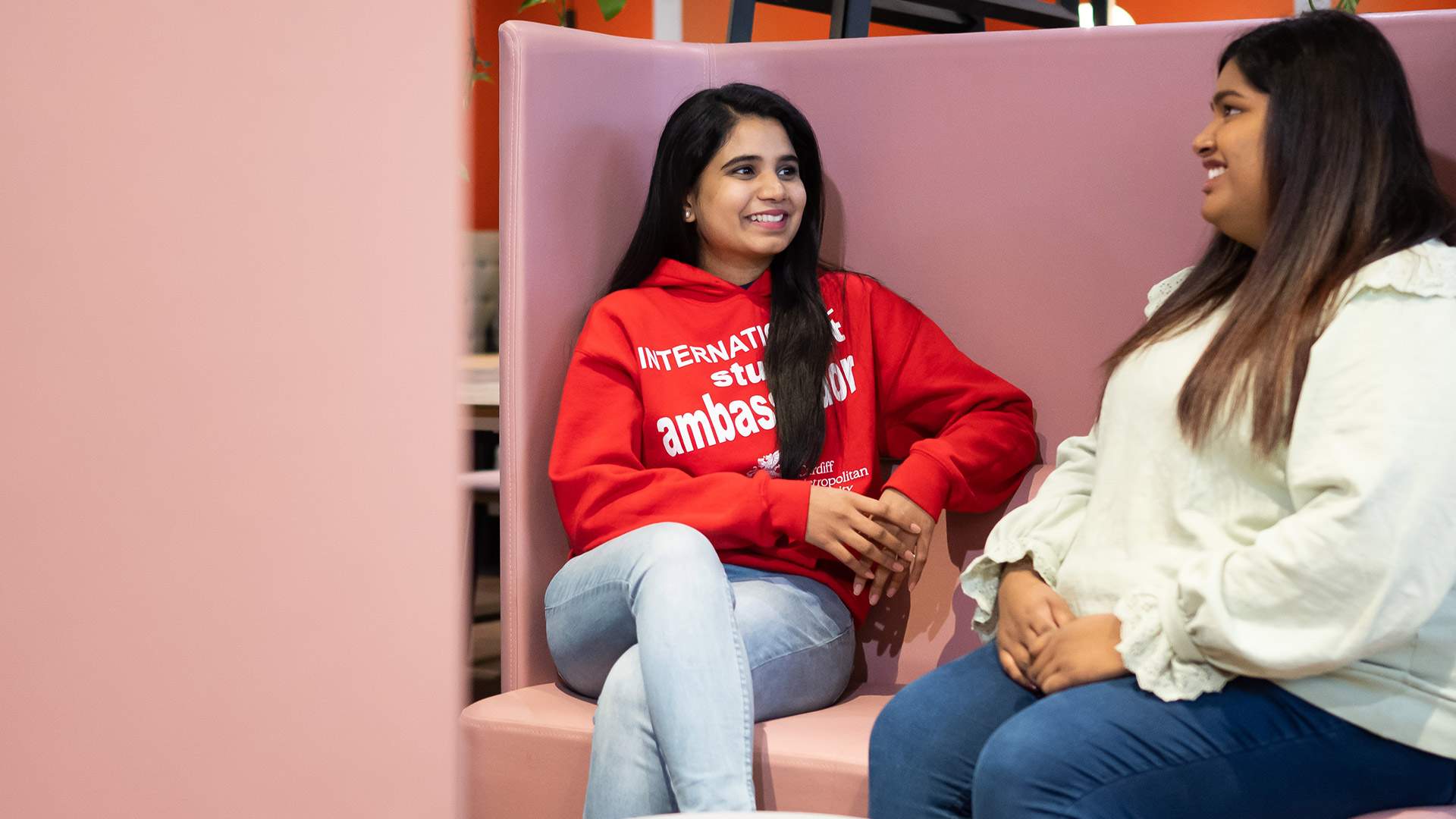 Two women engaged in conversation while seated on a pink couch, creating a warm and inviting atmosphere.