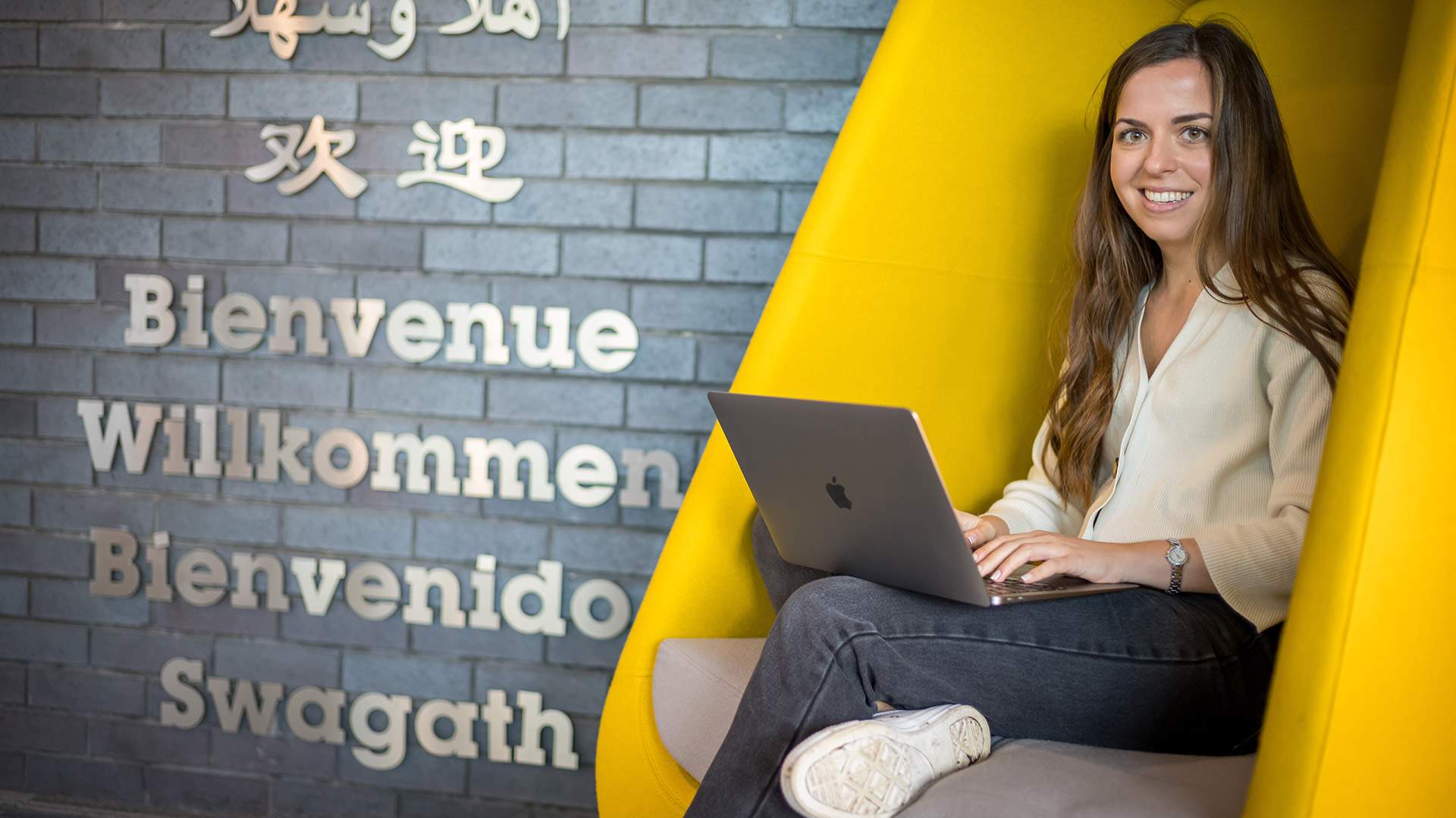 A woman working on her laptop while comfortably seated in a bright yellow chair, showcasing a lively atmosphere.