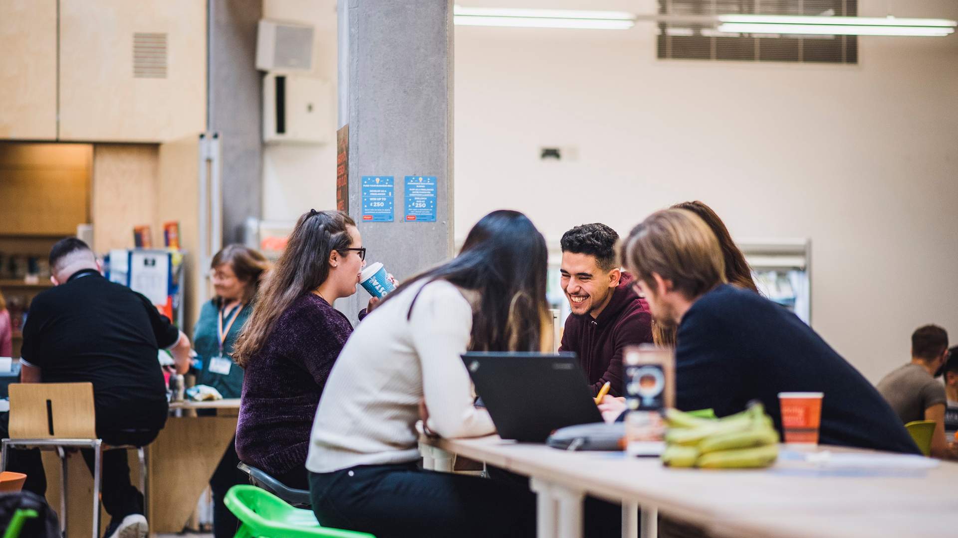 Five young adults sit around a table in an open cafe area