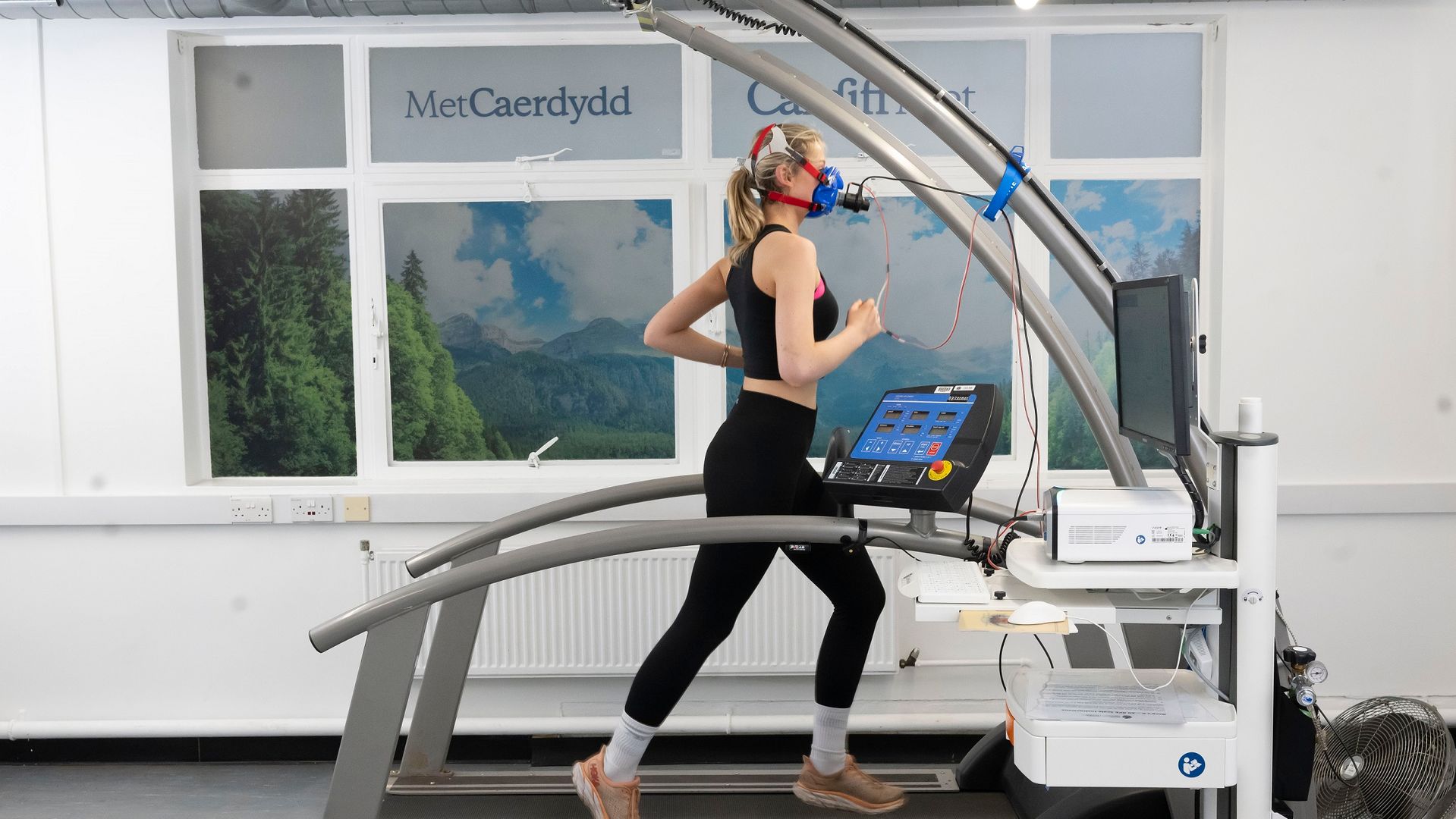 A young woman runs on a treadmill while wearing a breathing mask to measure her core vitals