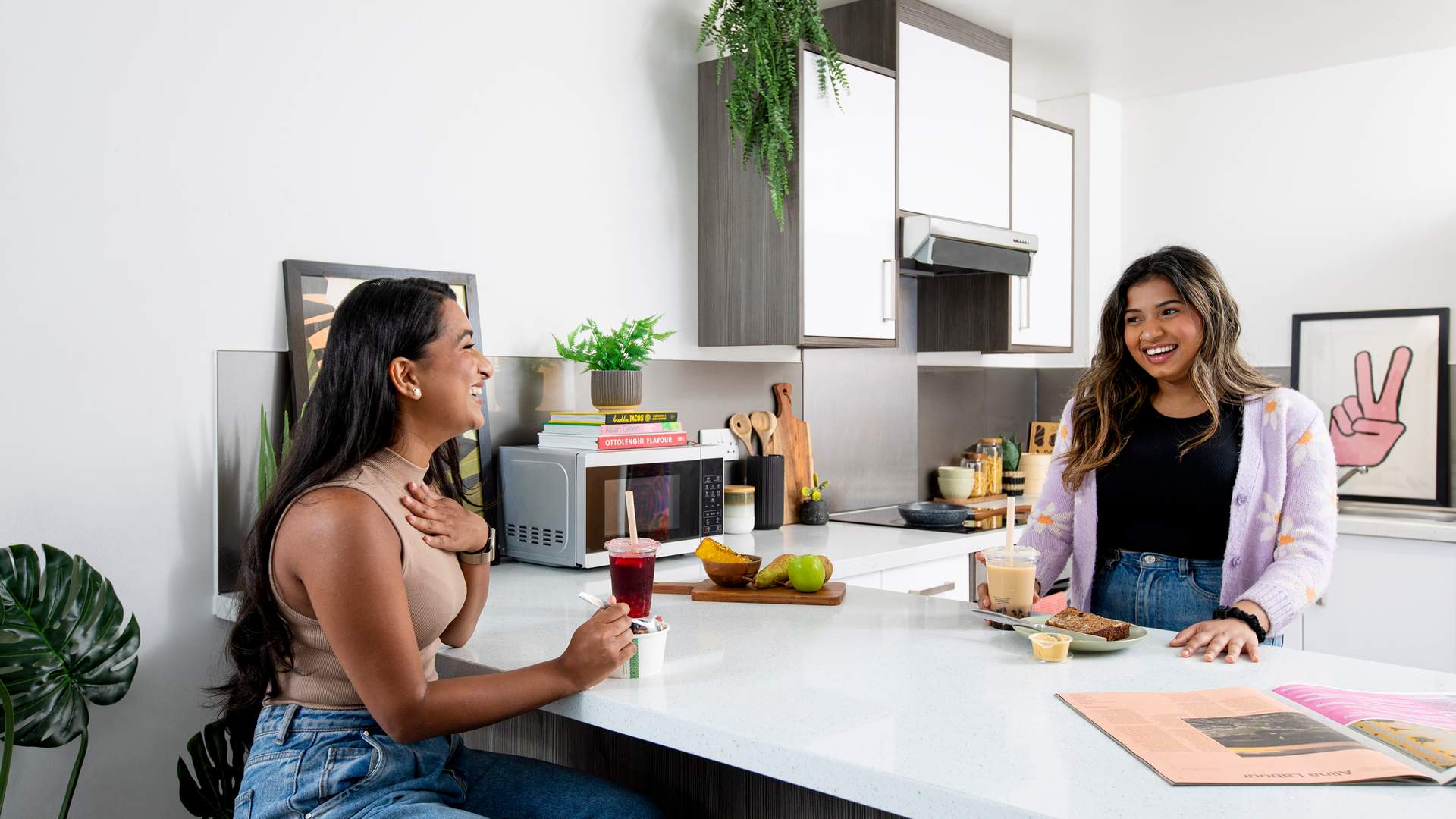 Two young adults sitting and talking at a kitchen island while preparing food