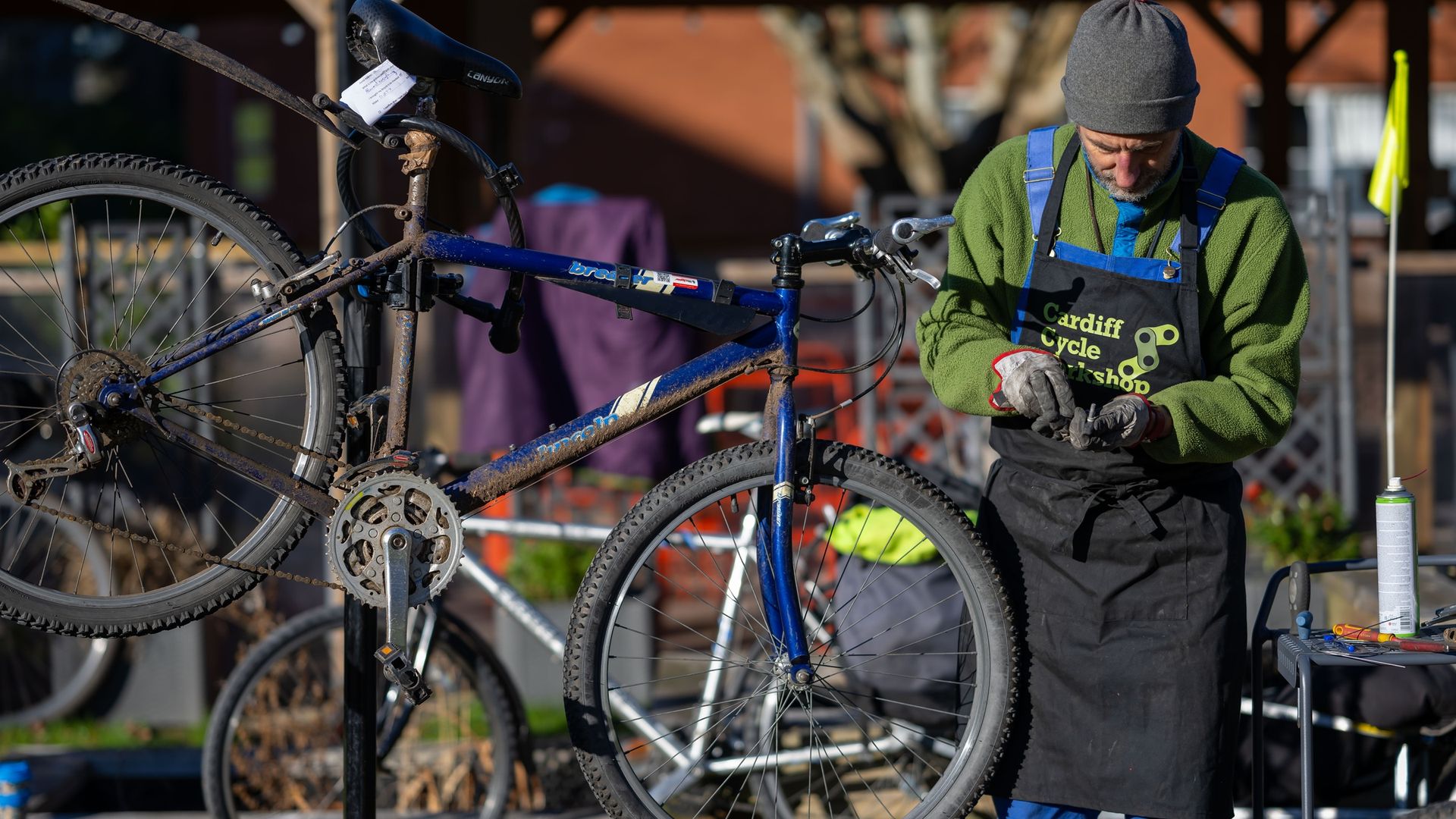 A man inspects a metal bolt in his hands while repairing a bicycle raised on a stand
