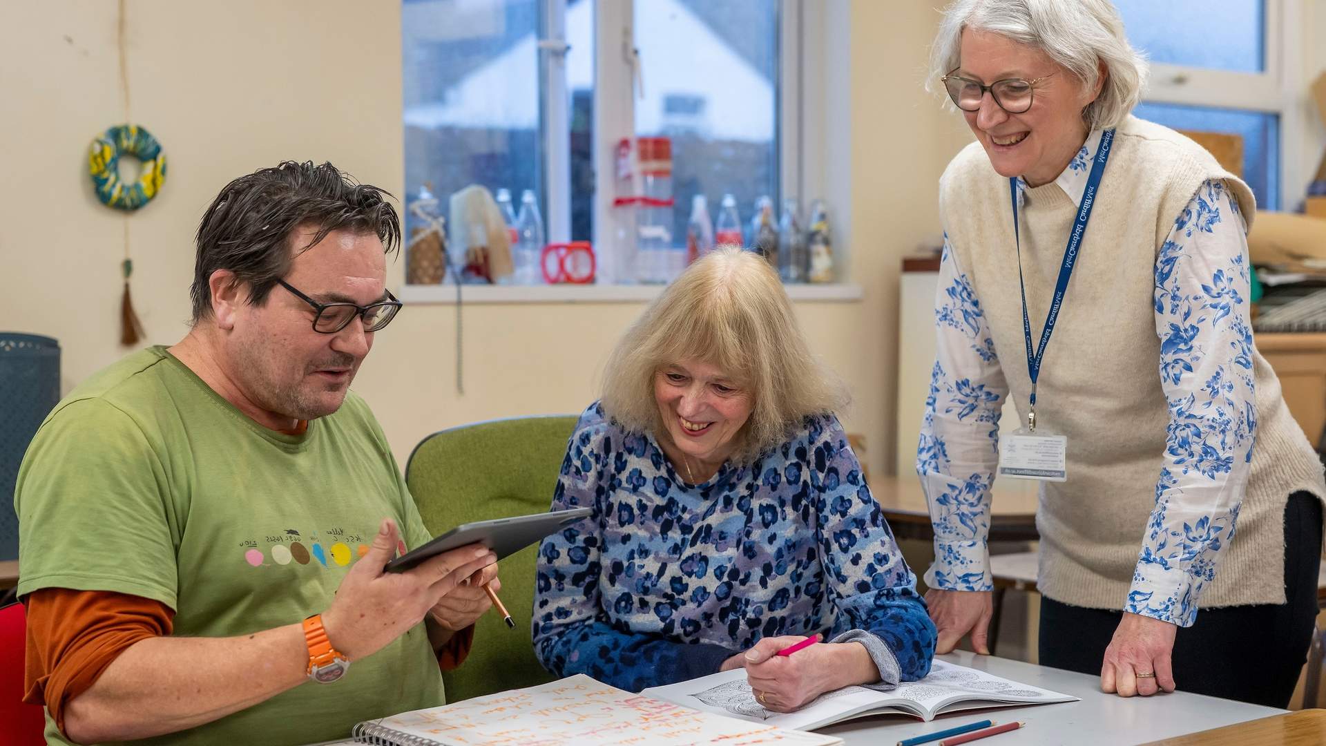 Adult students work from an electronic tablet overseen by a member of Cardiff Met staff