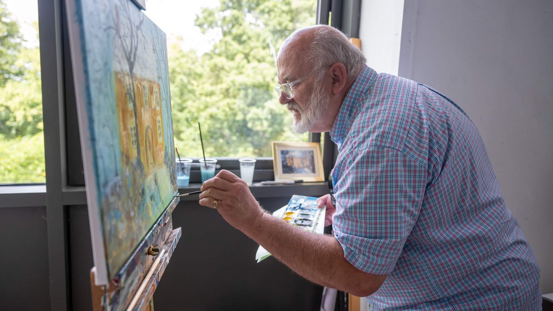 An elderly man in a short sleeve shirt paints on a large canvas