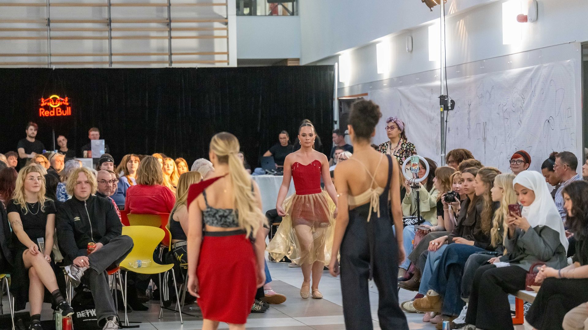A fashion catwalk in a large open space, surrounded by sitting attendees