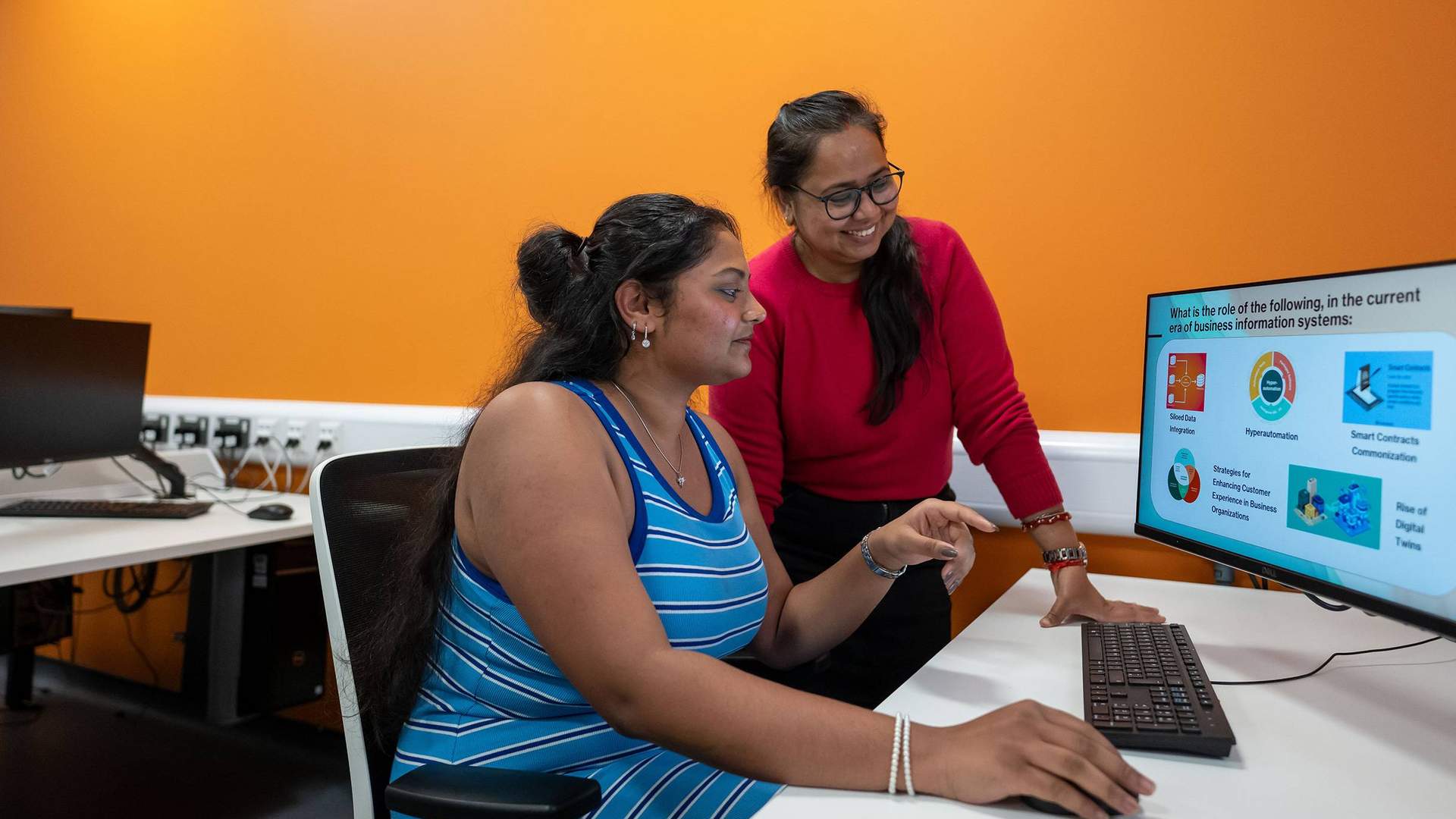 Two people collaborating in front of a computer screen, engaged in discussion and reviewing information together.
