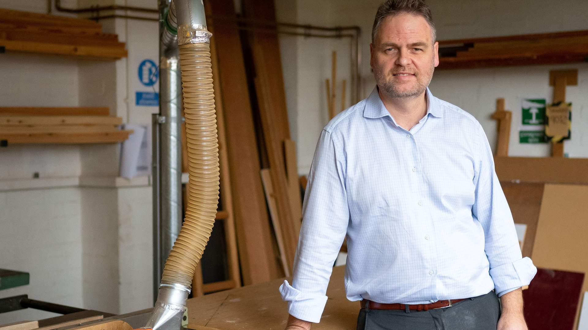 A teacher stands in a room, surrounded by woodworking equipment and tools.
