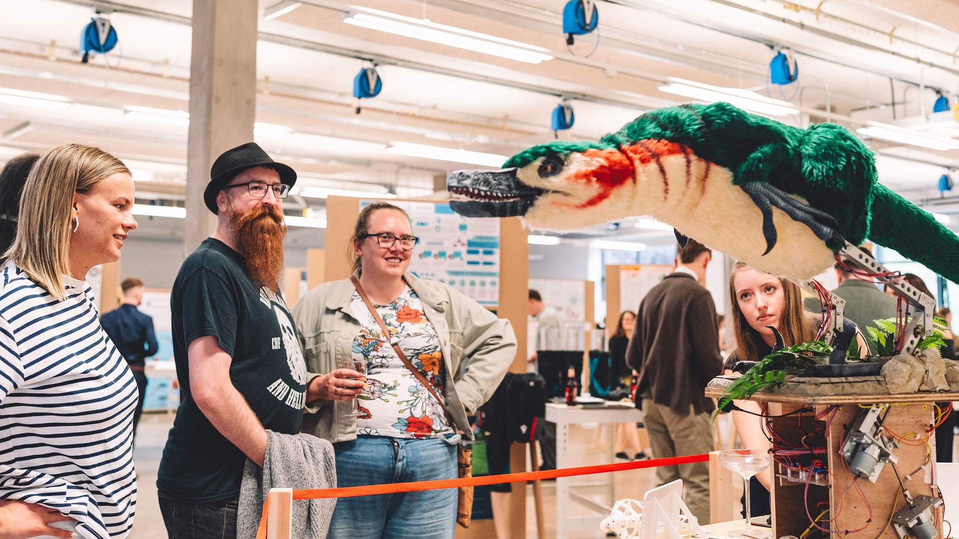 A group of people view a mechanical model of a prehistoric bird. The bird is standing on a pedestal with motors and wires visible beneath.