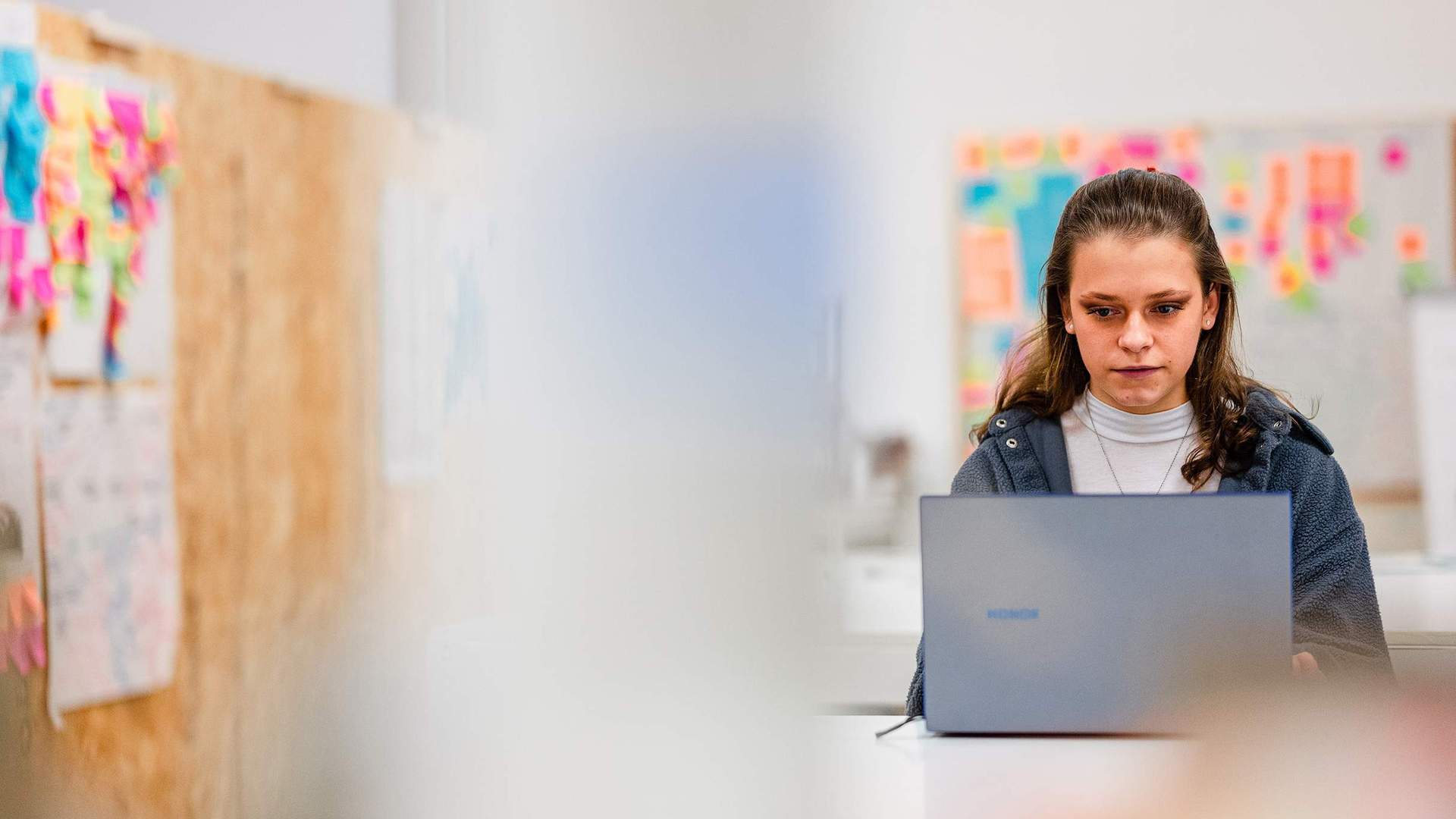 A young adult works from a laptop in an arts workspace.