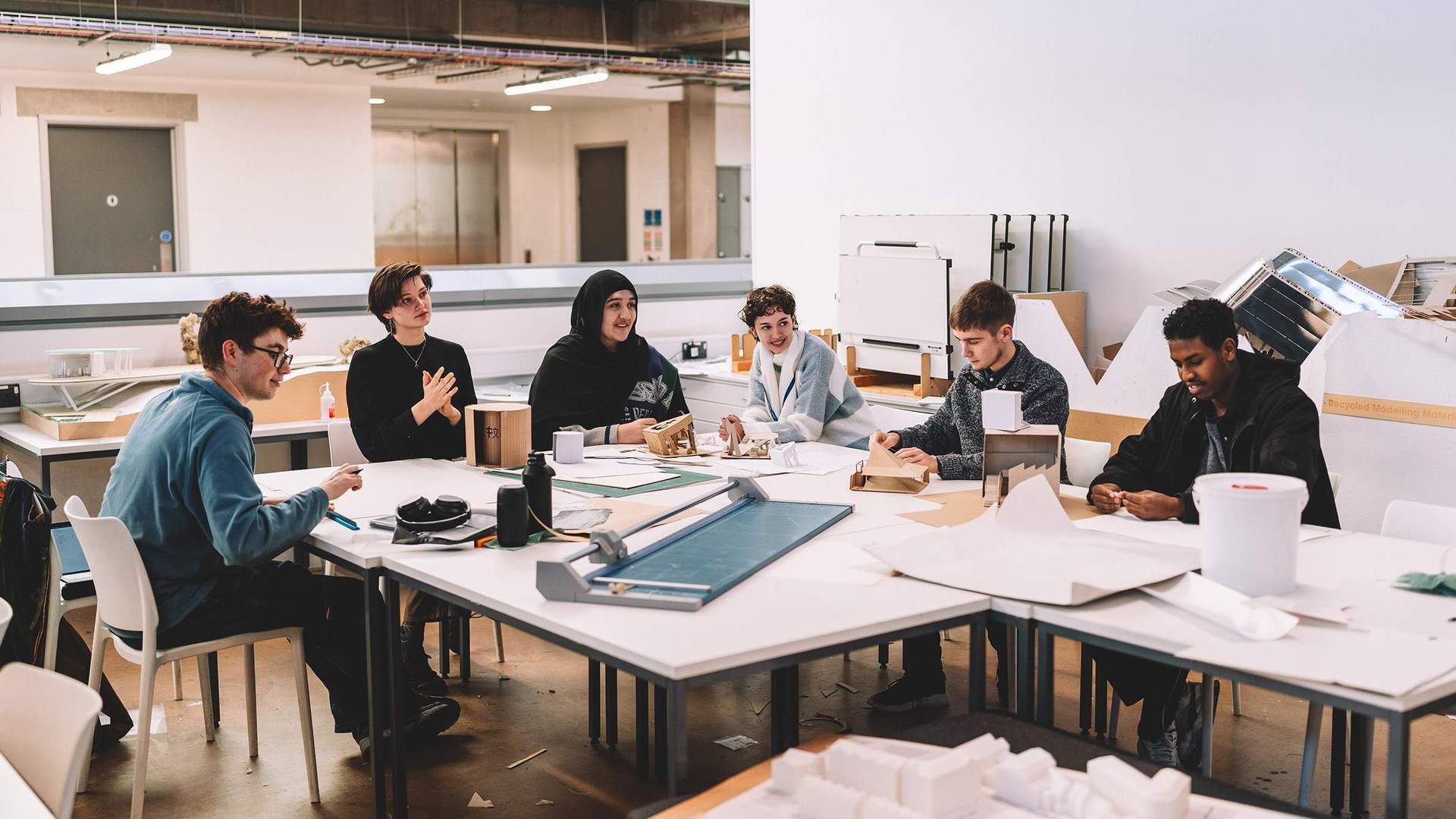 Group seated around studio tables examining models and papers in a large workspace.