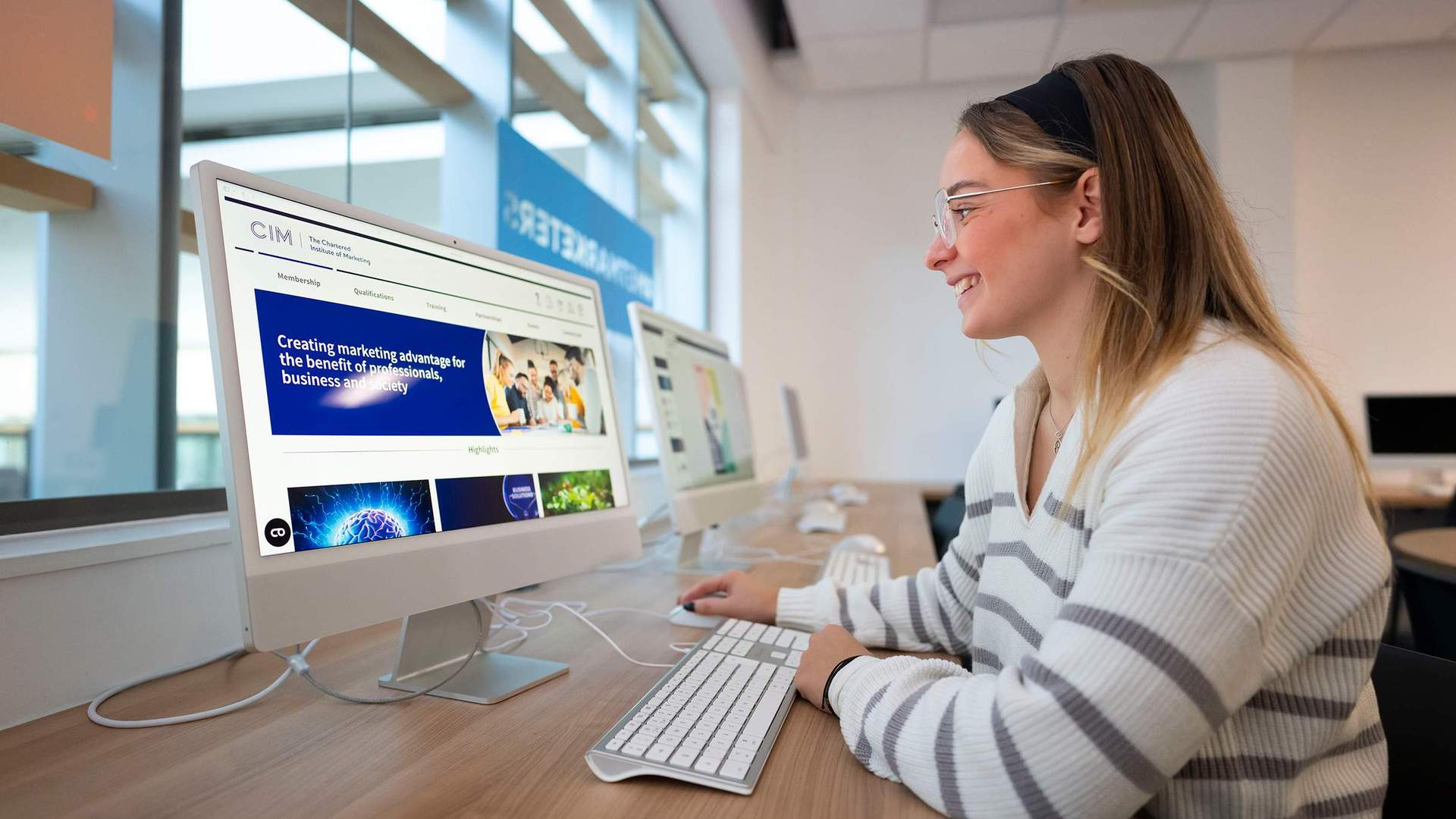 A person sat at a desk in front of a Mac computer.