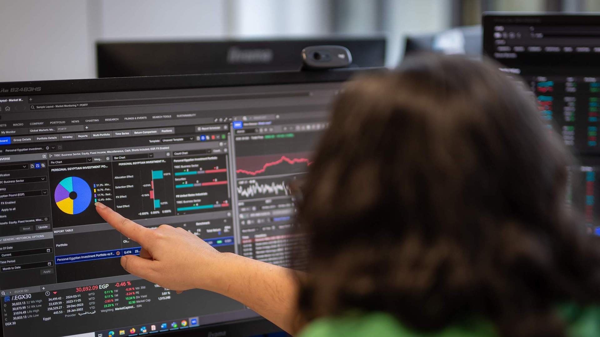 A person points to a large computer monitor showing financial charts.