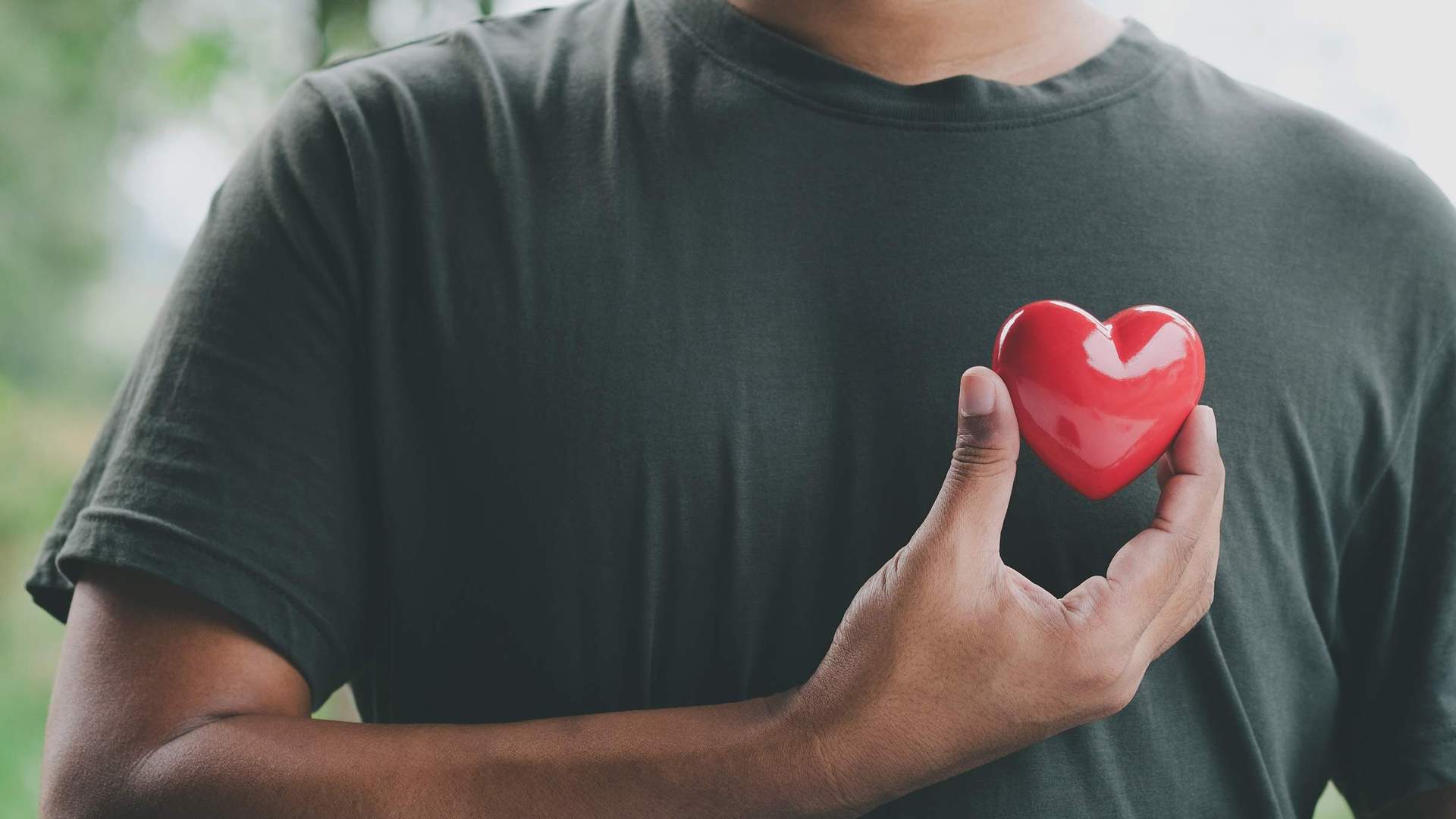 A man holding a small red heart against his chest.