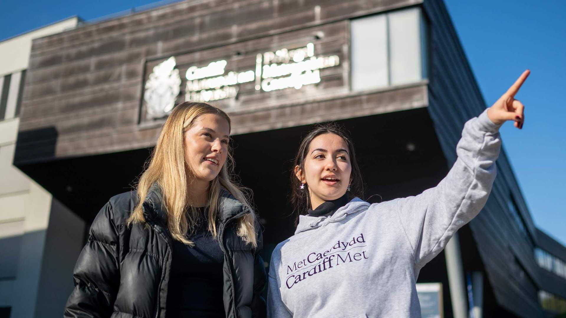 A Student Ambassador giving directions to an Open Day visitor outside the Cardiff School of Management building.