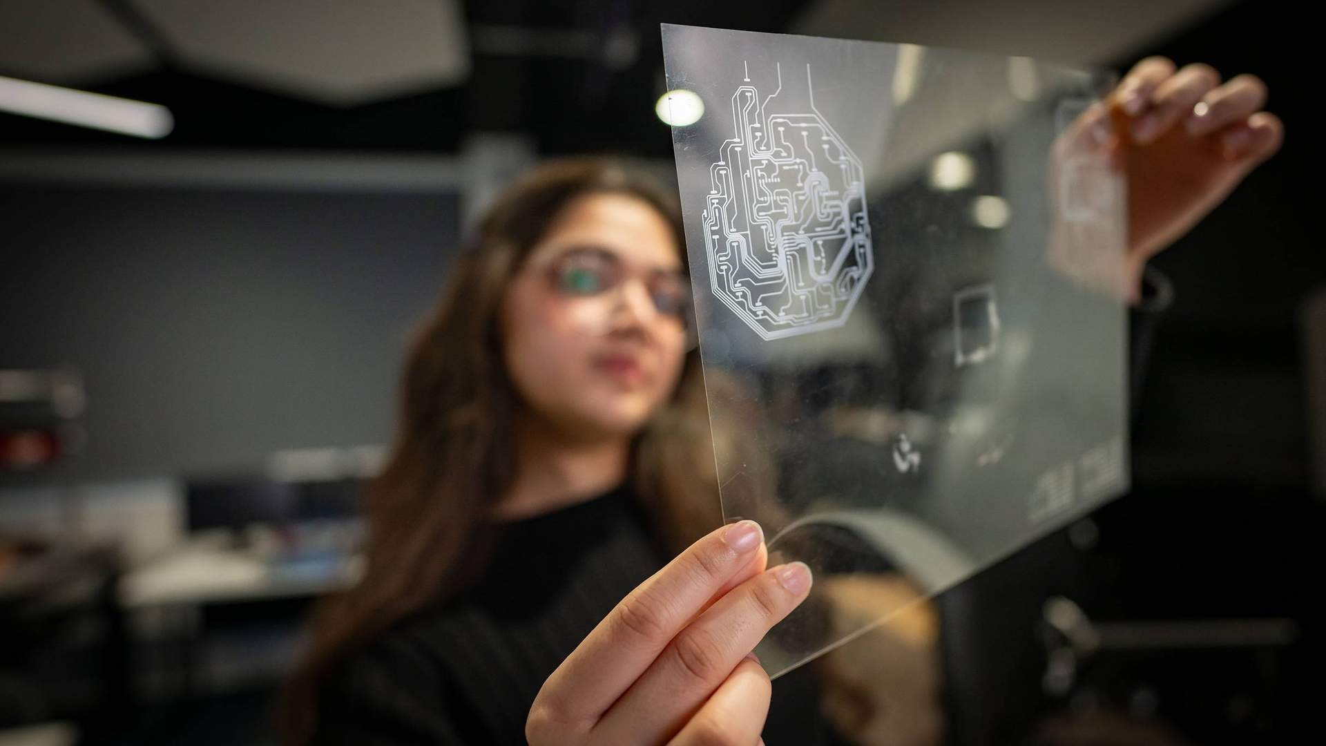 A person holds a small transparent sheet, etched with electronic circuits.