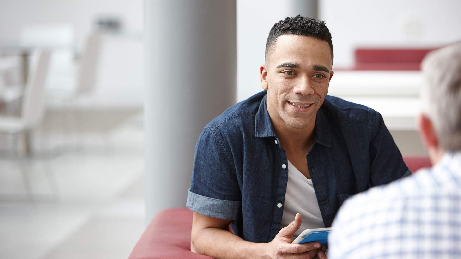 A man holding an iPad while engaged in conversation with another person.