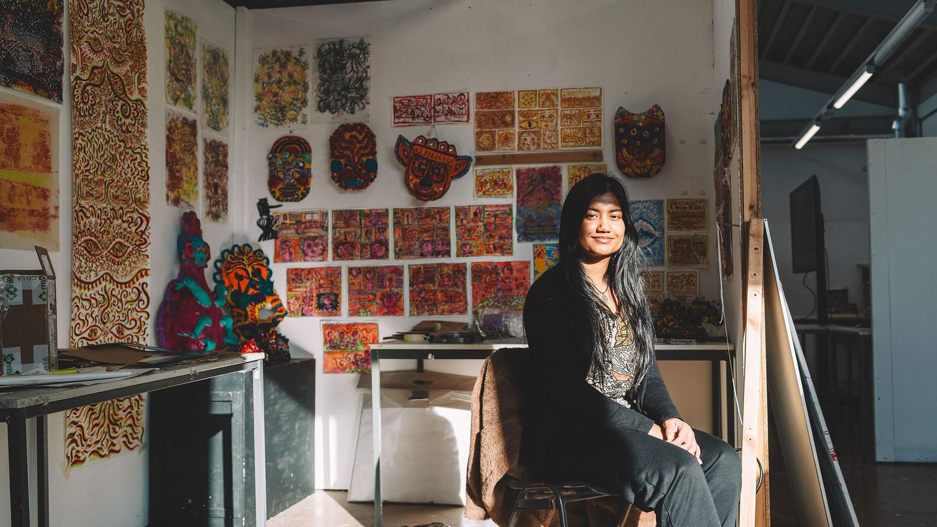 A student sits in front of a wall filled with various pieces of colourful artworks.