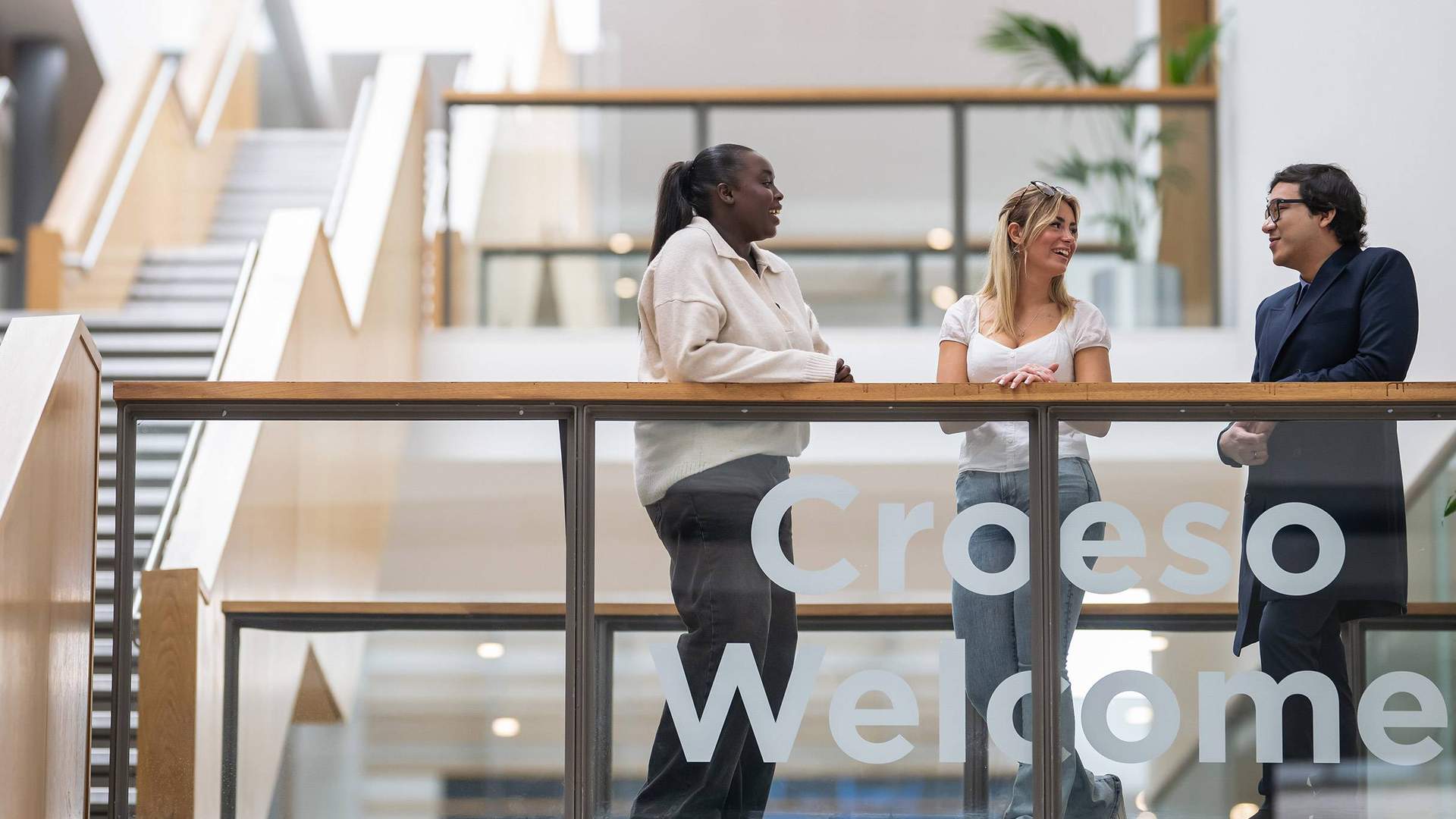Three people talking to each other on a balcony in an atrium space.