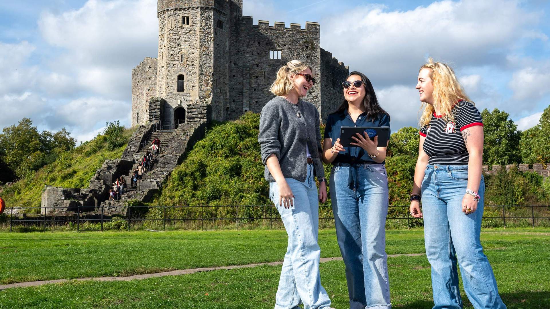 Three people stand together in front of a large, historic castle keep.