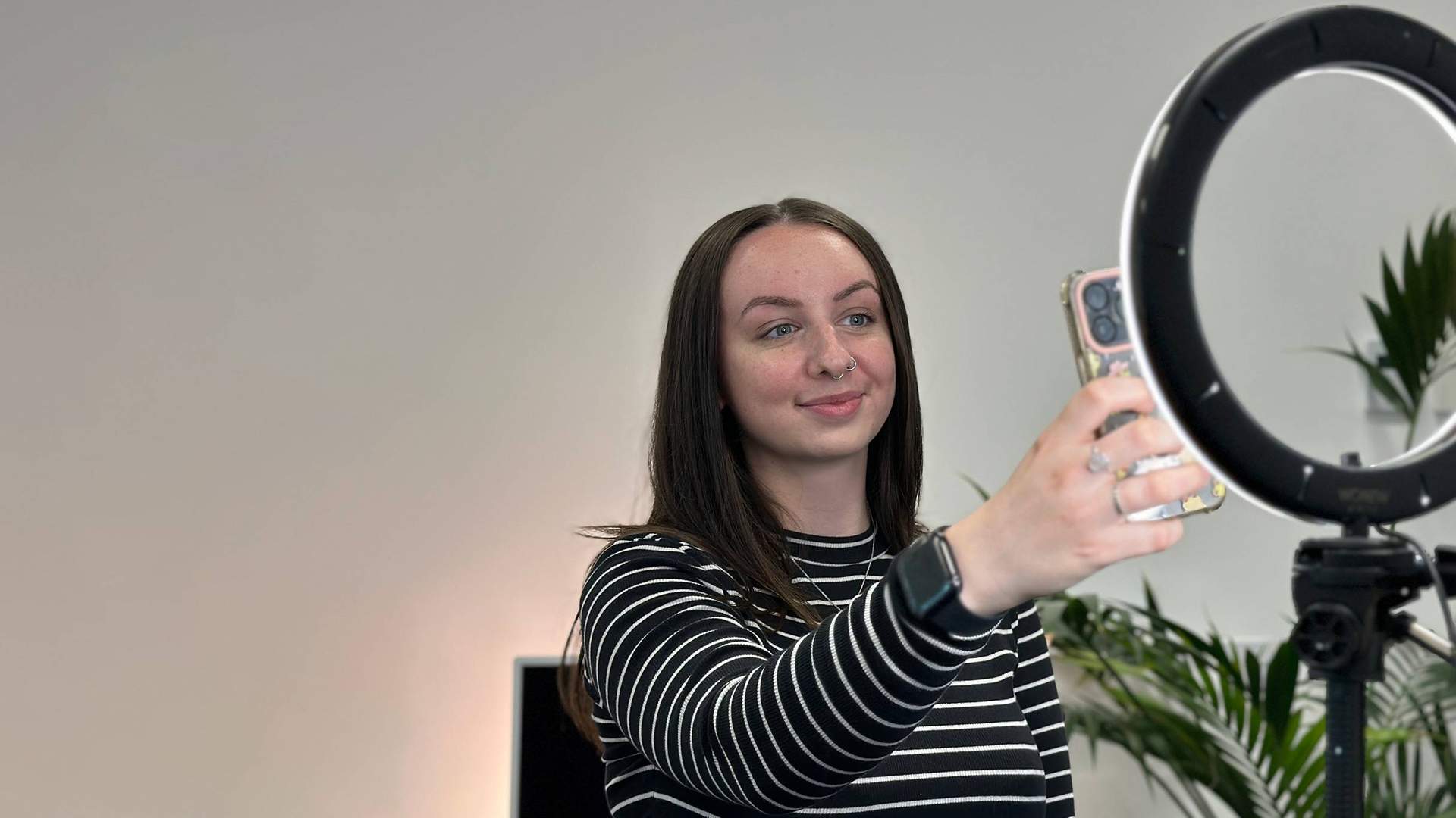 A person filming themselves using a mobile, illuminated by a ring light.