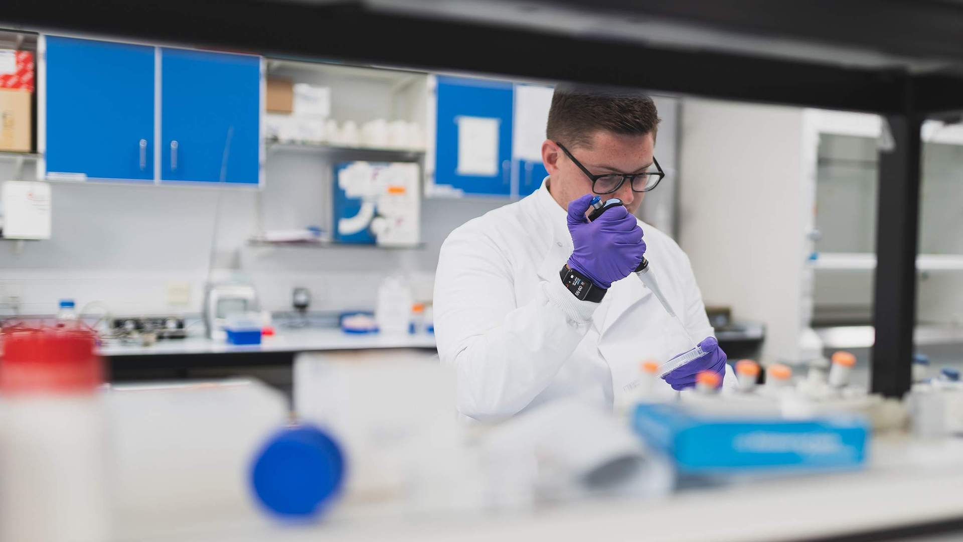 A person in a lab coat uses a pipette to dispense a sample into a container.