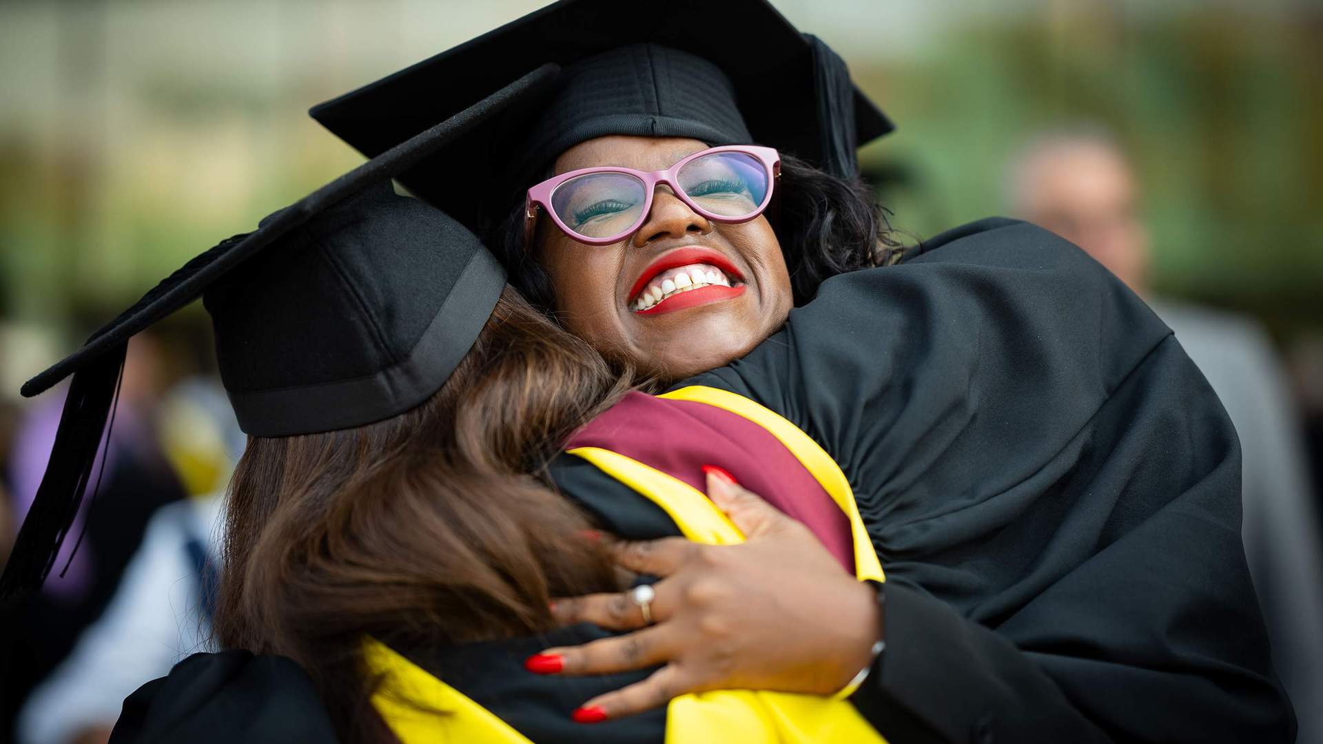 Two students in graduation caps and gowns hug each other.