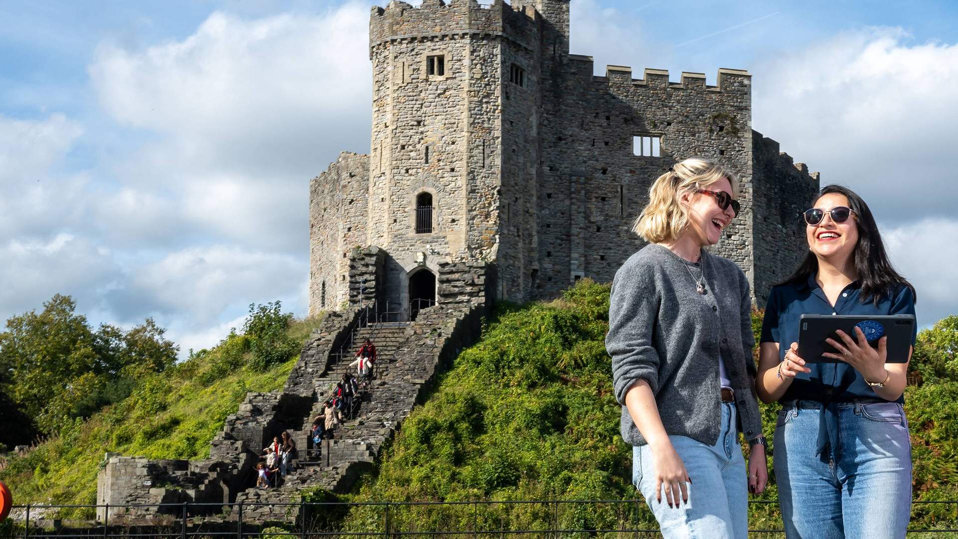 Two people stand together in front of a large, historic castle keep.