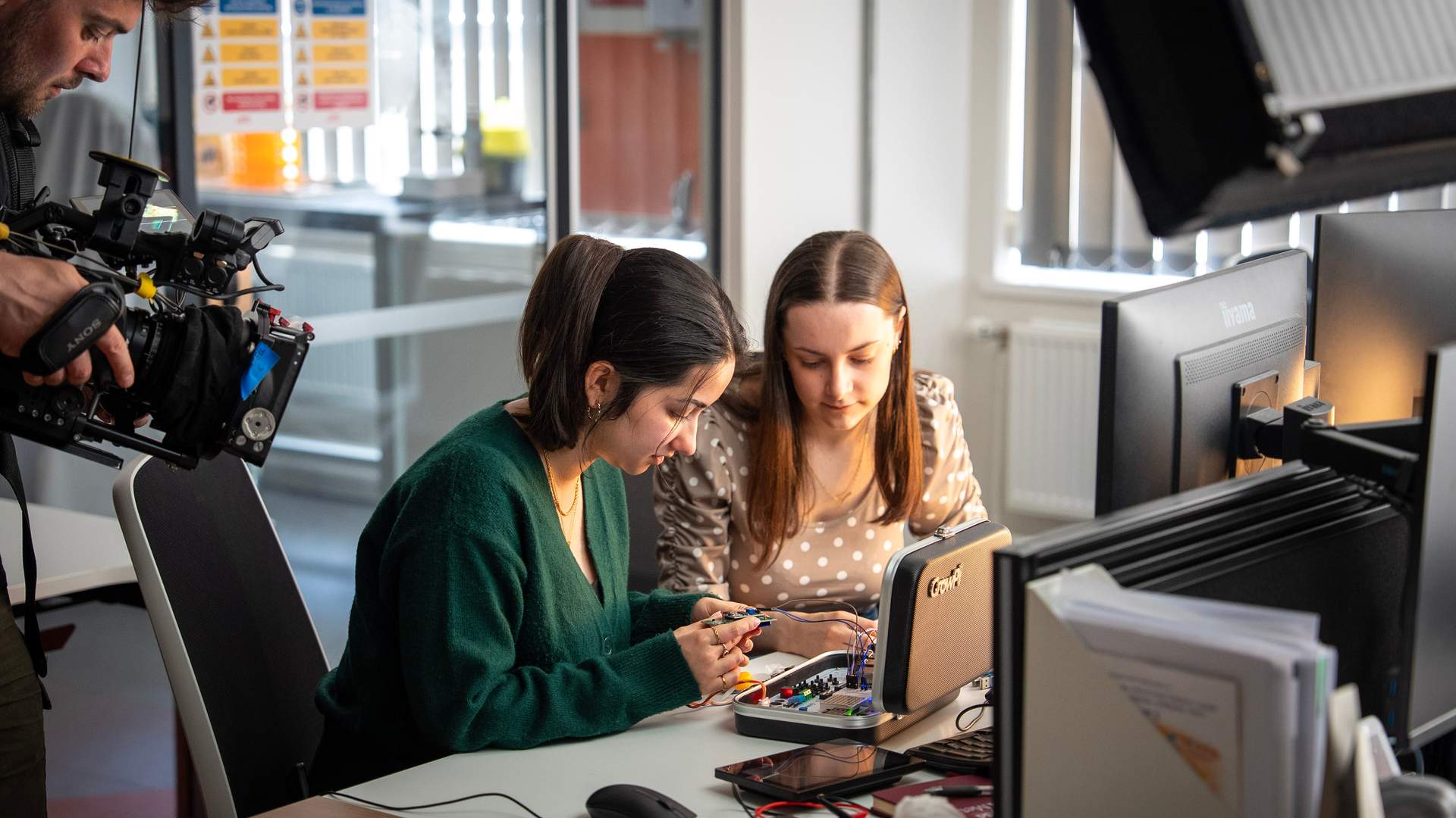 Two students work on a circuit board sat at a computer desk