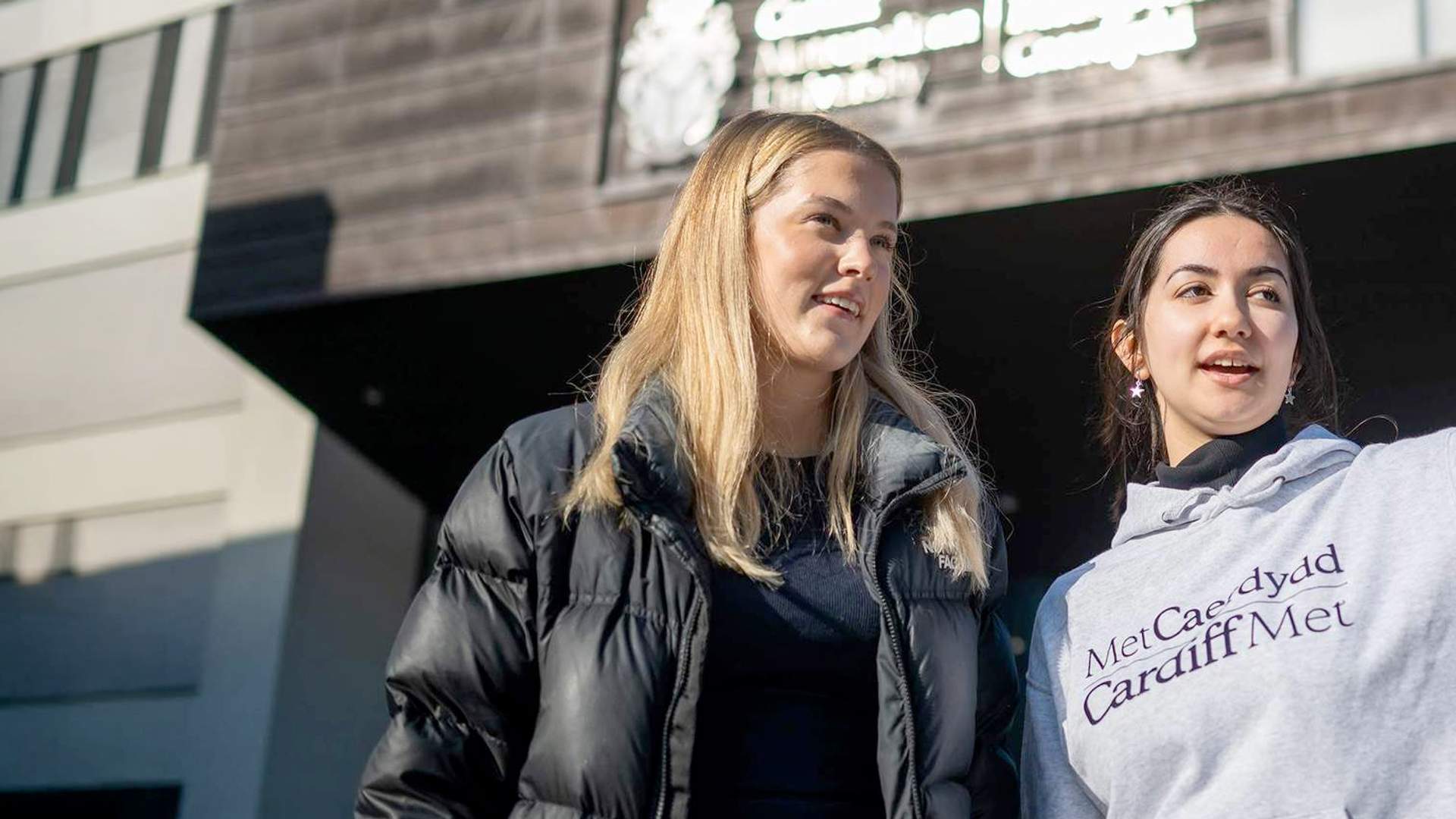A Student Ambassador giving directions to an Open Day visitor outside the Cardiff School of Management building.