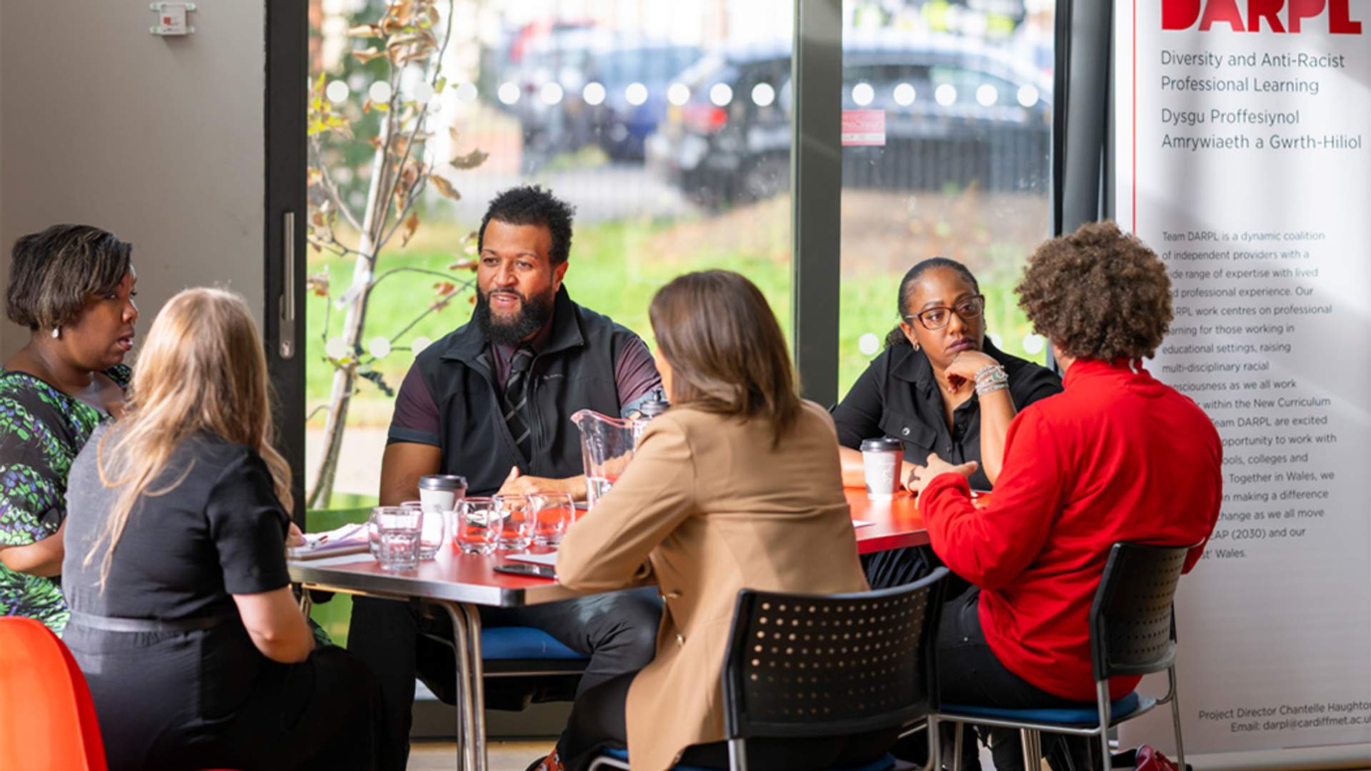 A group of people are sitting around a table. A banner with DARPL on it is visible in the background.