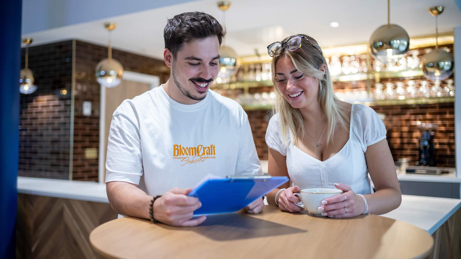 Aerial view of a vibrant waterfront city with winding rivers, numerous buildings, and a marina. The landscape features green spaces and urban areas under a clear blue sky.