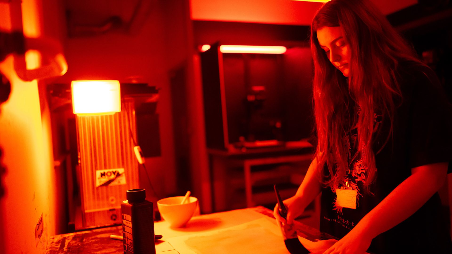 Two people in a photography studio look at a cameras screen, smiling. They stand close together, with lighting equipment visible in the background. One person wears a green cap and holds the camera.