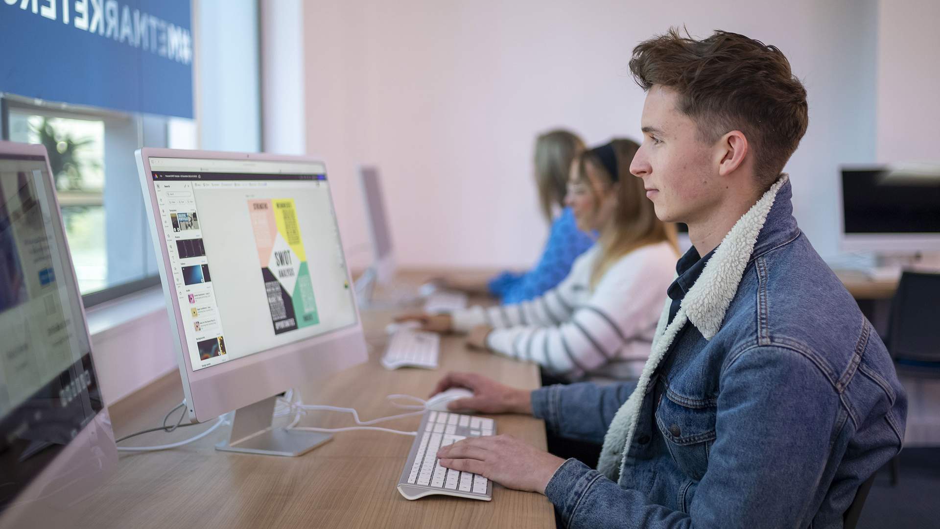 A man with glasses and a mustache is smiling while using a laptop outdoors. He is wearing a green shirt and is surrounded by a blurred, sunny background of trees and greenery.