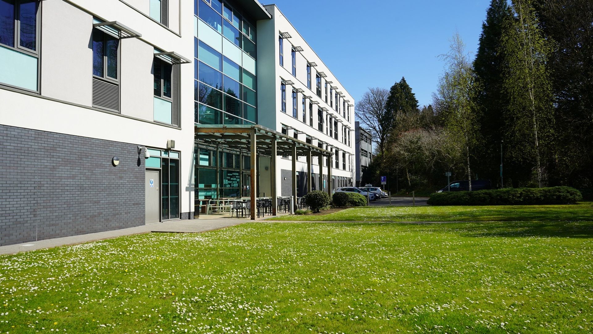 Rear view of the Cardiff School of Management, including an open green space and outdoor seating, on a sunny day