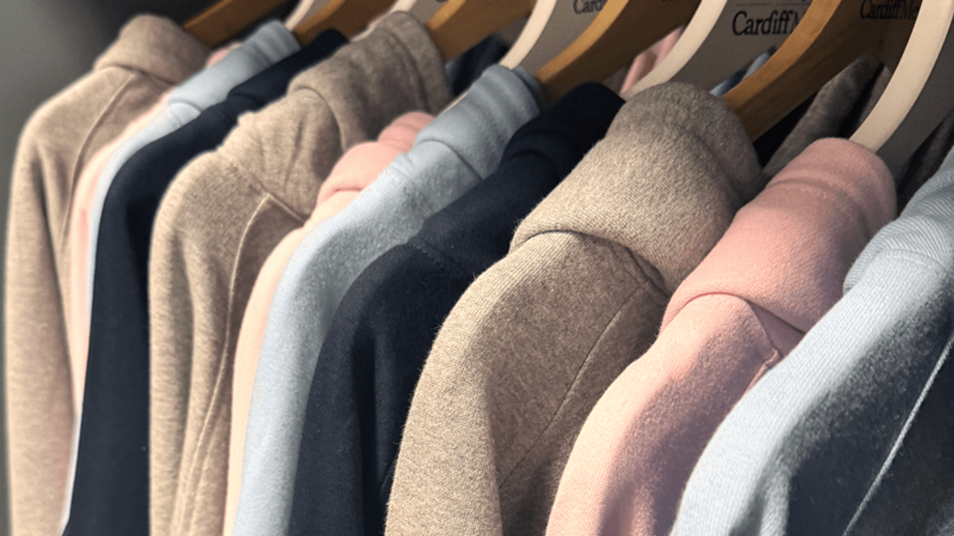 A row of Cardiff Met-branded hoodies and sweatshirt lined up on a clothes rail