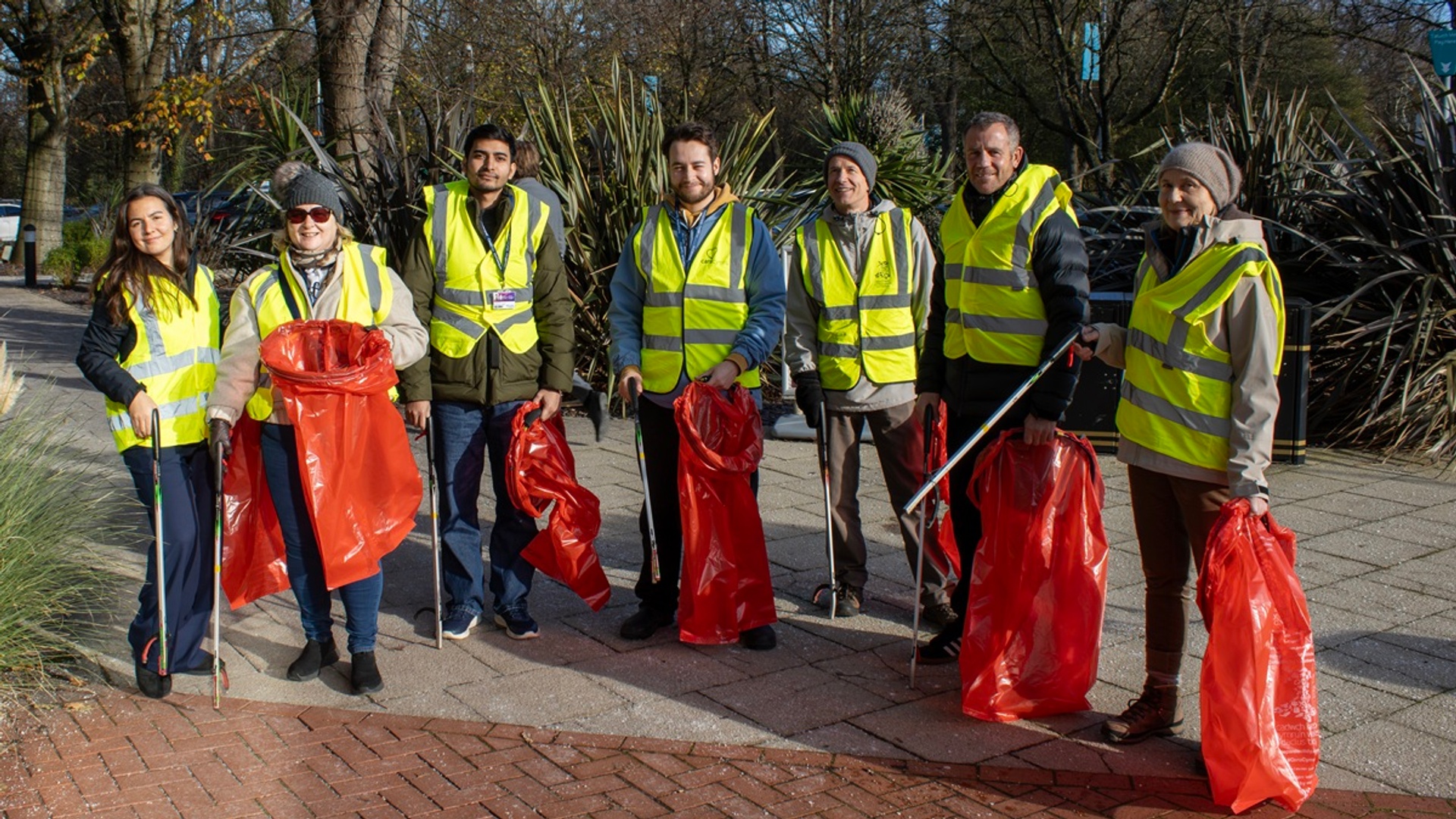 A group of litter pickers in high visibility vests hold waste bags and litter picking sticks