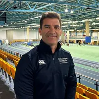 Gareth Baber poses in front of a spacious indoor track, showcasing the athletic environment around him.