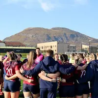 A group of women rugby players huddle together on the field, discussing strategy during a match.