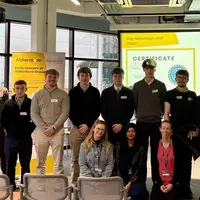 Several individuals gather in front of a screen, likely participating in a meeting or presentation.