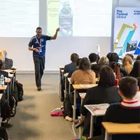 A man stands before a group, giving a presentation and interacting with attendees.