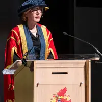 A woman in a graduation gown and cap delivers a speech at a graduation ceremony.