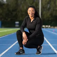 Cardiff Met student in black sportswear crouches on running track