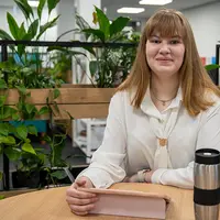 A woman at a table with greenery, sipping coffee and relaxing in a cozy setting.