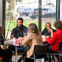 A group of people are sitting around a table. A banner with DARPL on it is visible in the background.