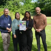 n a park, four people hold a certificate, smiling and celebrating their achievement together.