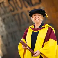 A woman in a graduation gown and cap proudly holds her diploma, celebrating her academic achievement.