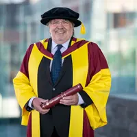 A man in a suit wearing academic robes and cap.