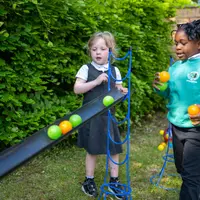 Two kids happily tossing balls back and forth in a sunny yard filled with green grass.