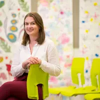 A research student sits sideways on a lime green chair in a room featuring colourful floral wall designs